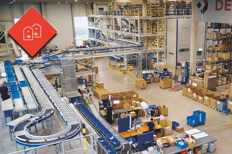 Ein geräumiges Lager mit mehreren Förderbändern, die Pakete transportieren, zeigt das technische Sortiment von DEXIS Austria. Zahlreiche Regale sind mit verschiedenen Artikeln bestückt, und Mitarbeiter verwalten die Abläufe an verschiedenen Stationen. In der oberen linken Ecke ist eine rote Raute mit einem Tag-Symbol eingeblendet.