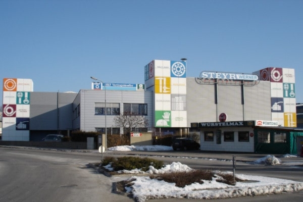 Das Geschäftsgebäude präsentiert farbenfrohe geometrische Tafeln und das Firmenlogo „STEYR WERNER“ vor schneebedecktem Boden und strahlend blauem Himmel.