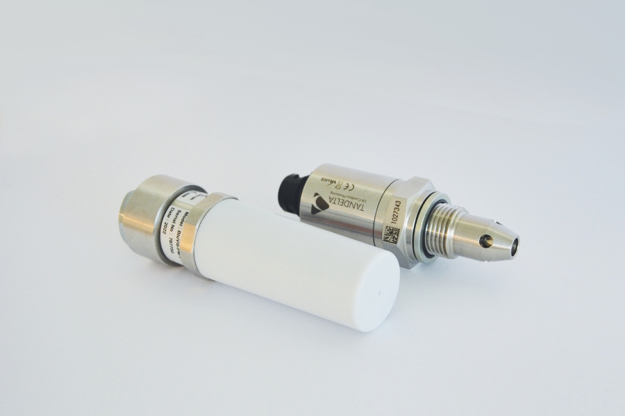 Zwei Predictive Maintenance Industriesensoren mit metallischem Gehäuse und Branding. Ein Sensor ist aus Metall, während der andere ein weißes zylindrisches Gehäuse besitzt. Beide sind auf einer schlichten weißen Oberfläche platziert.
