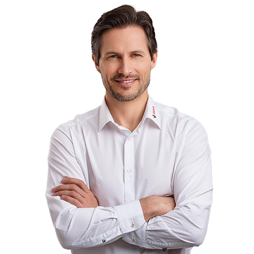 DEXIS Experte in weißem Hemd Ein Mann mit dunklem Haar und Bart steht lächelnd mit verschränkten Armen da. Er trägt ein weißes Oberhemd mit einem Logo am Kragen.