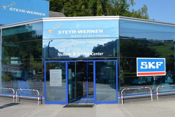 Vorderansicht des Steyr-Werner Technik & Service-Centers in Waidhofen an der Ybbs mit einer Glasfassade, in der sich Grünpflanzen spiegeln. Ein großes SKF-Logo ziert die rechte Seite.