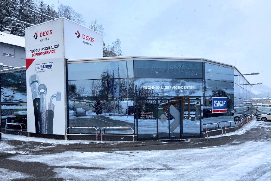 Modernes Glasgebäude von DEXIS Austria in Waidhofen an der Ybbs mit der Aufschrift „Technik & Service Center“. An der Fassade befinden sich Logos von DEXIS Austria und SKF. Schnee bedeckt den Boden.