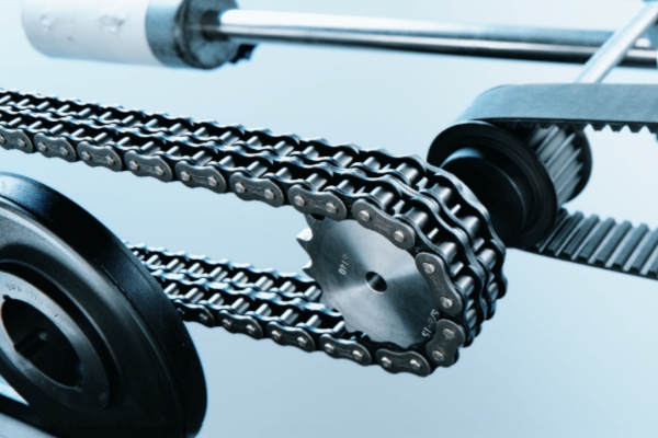 Nahaufnahme einer Metallrollenkette um ein Kettenrad und einem Riemen auf Riemenscheiben. Vor hellblauem Hintergrund hebt das Bild die metallische Textur der Zahnräder hervor.